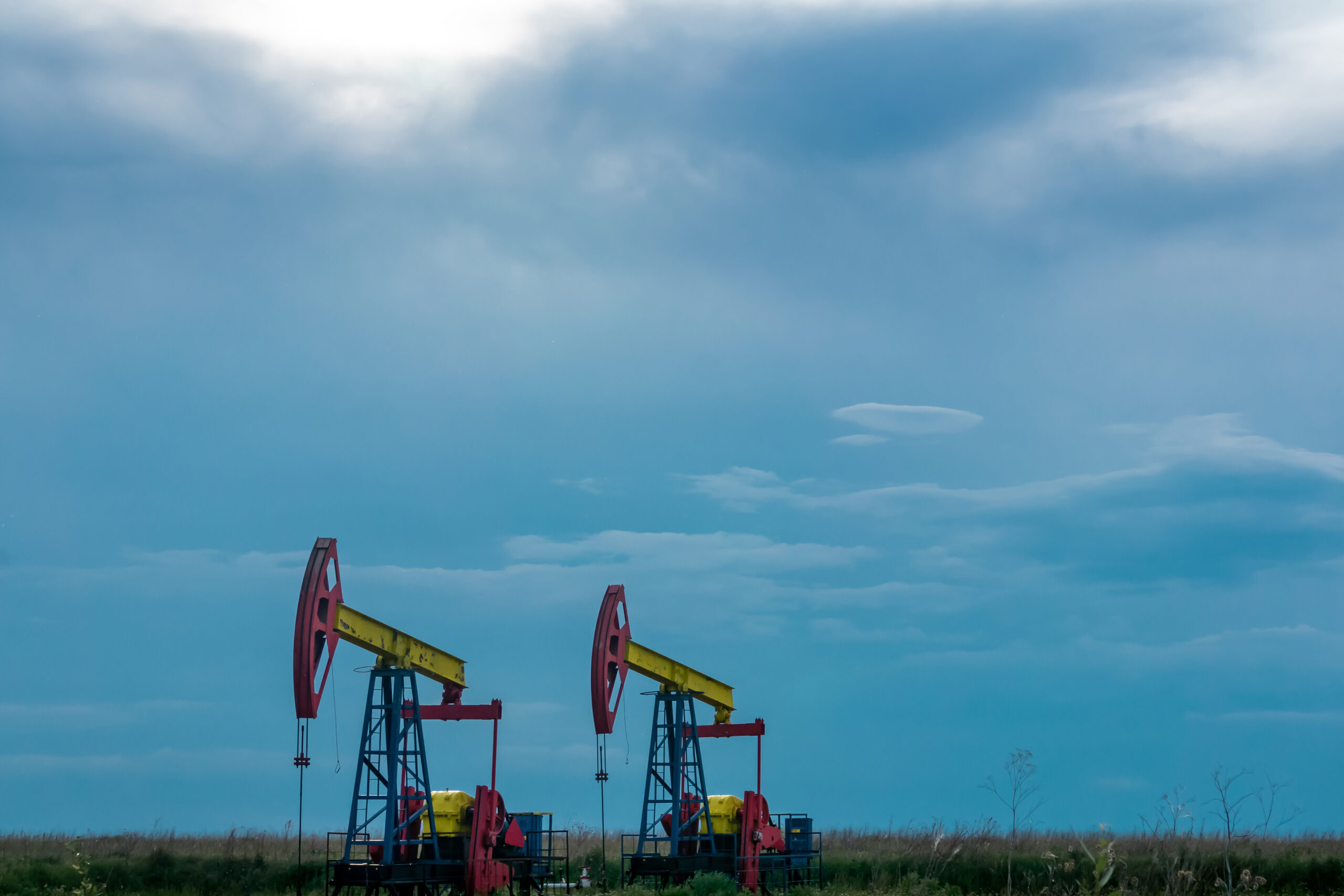 pumpjacks piston pumps operating at an oil well in field under cloudy sky